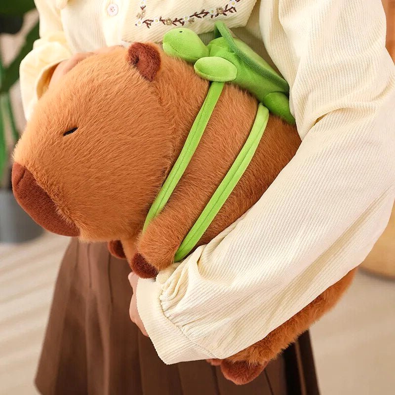 Close-up of arms holding a Capybara Dreams plush backpack toy, showcasing its soft fabric and the cute green turtle design backpack.