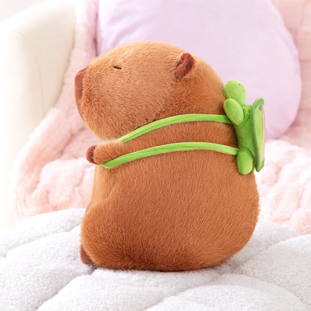 Side view of the Capybara Dreams plush backpack toy, showcasing the adorable green turtle design attached to its back, on a white surface.