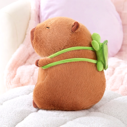 Side view of the Capybara Dreams plush backpack toy, showcasing the adorable green turtle design attached to its back, on a white surface.