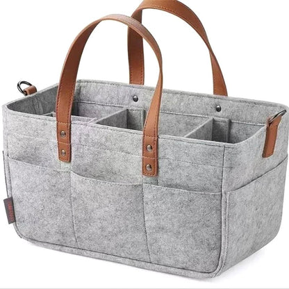 Angled view of the gray Cloudscape Diaper Tote Bag, made of structured felt with brown leather handles and multiple pockets, showcasing a small brand tag on the side.