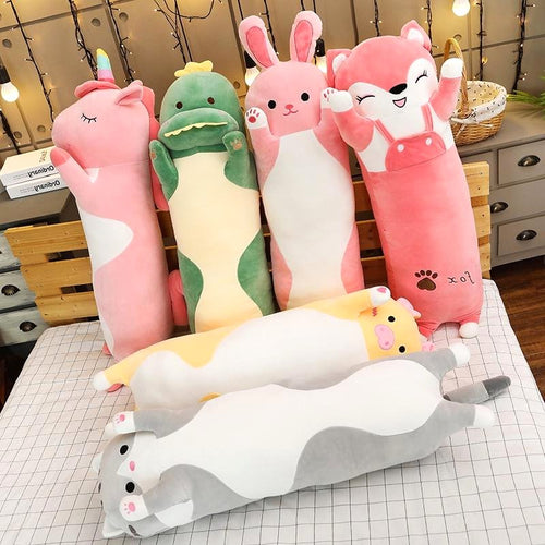 Cuddle Haven collection of long plush toys, including a pink fox, pink bunny, green dinosaur, pink unicorn, gray cat, yellow cat, displayed together on a bed. Showcases various soft fabric animal plushies.