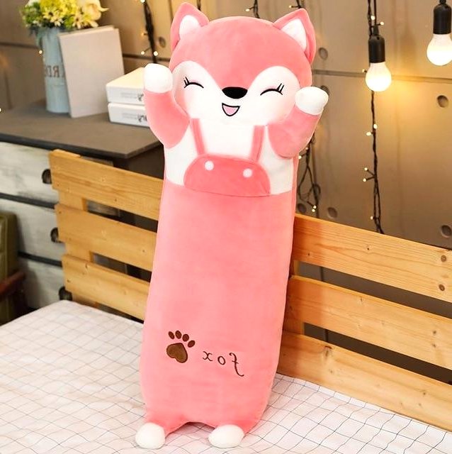 A long pink fox plush toy with a happy face and white belly stands upright on a bed, featuring a 'fox' text and paw print detail.