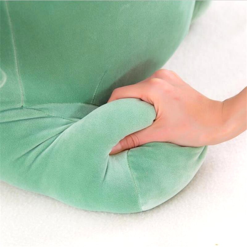 A close-up shot of a hand pressing into the side of a green dinosaur plush toy, highlighting its soft, squishy, and huggable texture.