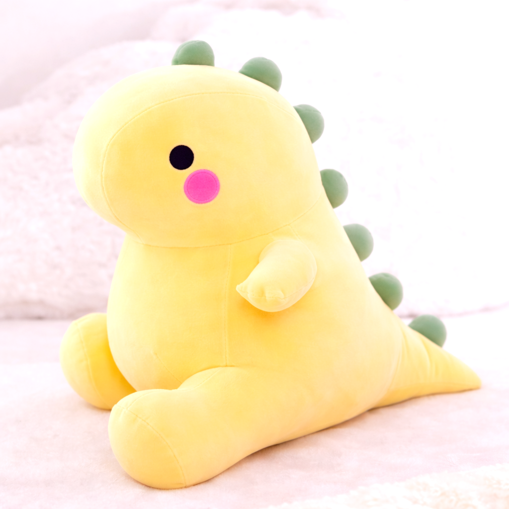 Yellow dinosaur plush toy with green spikes, soft fabric, adorable features, black eyes, and pink cheeks, sitting on a white textured background. Perfect for kids and collectors.