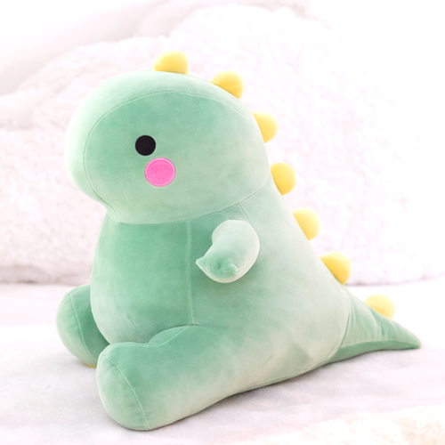 A single adorable green dinosaur plush toy made from soft fabric, featuring cute pink cheeks and yellow spikes, resting on a white textured surface.