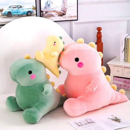 Three adorable dinosaur plush toys in soft fabric, featuring a large pink dino, a small yellow dino, and a large green dino, displayed on a cozy bed with decorative elements in the background.